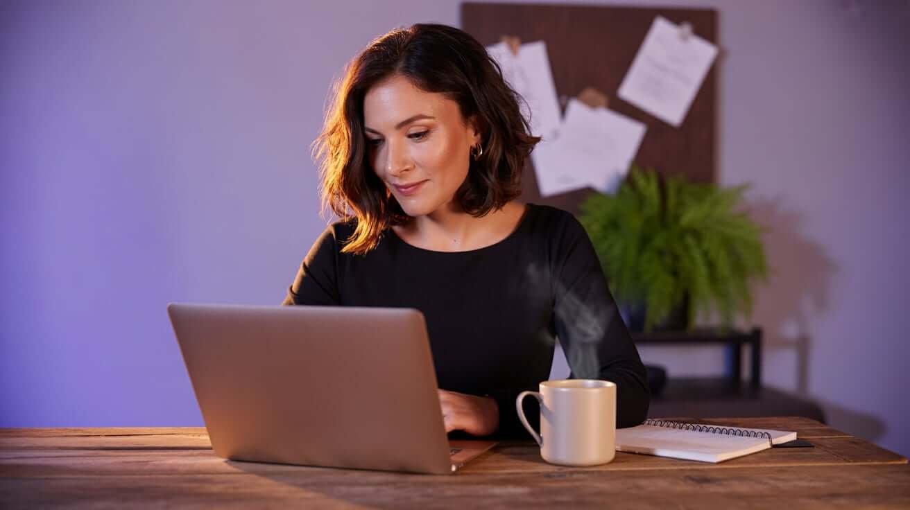 Junge HR-Beraterin bei einem Videoanruf in einem modernen Büro mit Laptop, Notizen und Kaffeetasse.